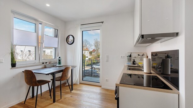 Cocina moderna con comedor, piso de madera y vista a través de la puerta de vidrio.