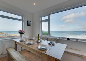 A dining area with a table set for four, large windows offering a view of the sea, and a picture on the wall. - 3 Bed in St. Ives (oc-trecar) (Saint Ives)