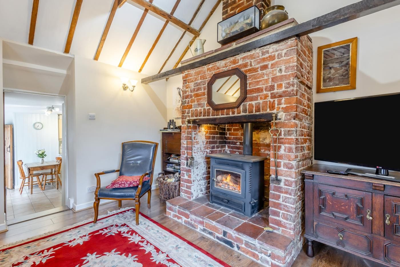 A room with a brick fireplace, a television, a wooden cabinet, a red and white rug, and a dining area with a table and chairs.