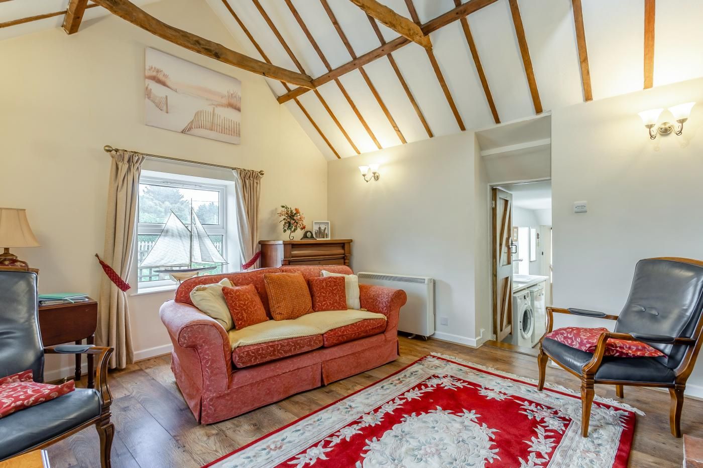A cozy living room with a red sofa, a patterned rug, and a wooden ceiling.