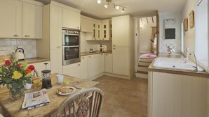 A kitchen with white cabinets, a double oven, a sink, and a dining area with a table set for breakfast. - 2 Bed in Aldeburgh (oc-marsh) (Friston)