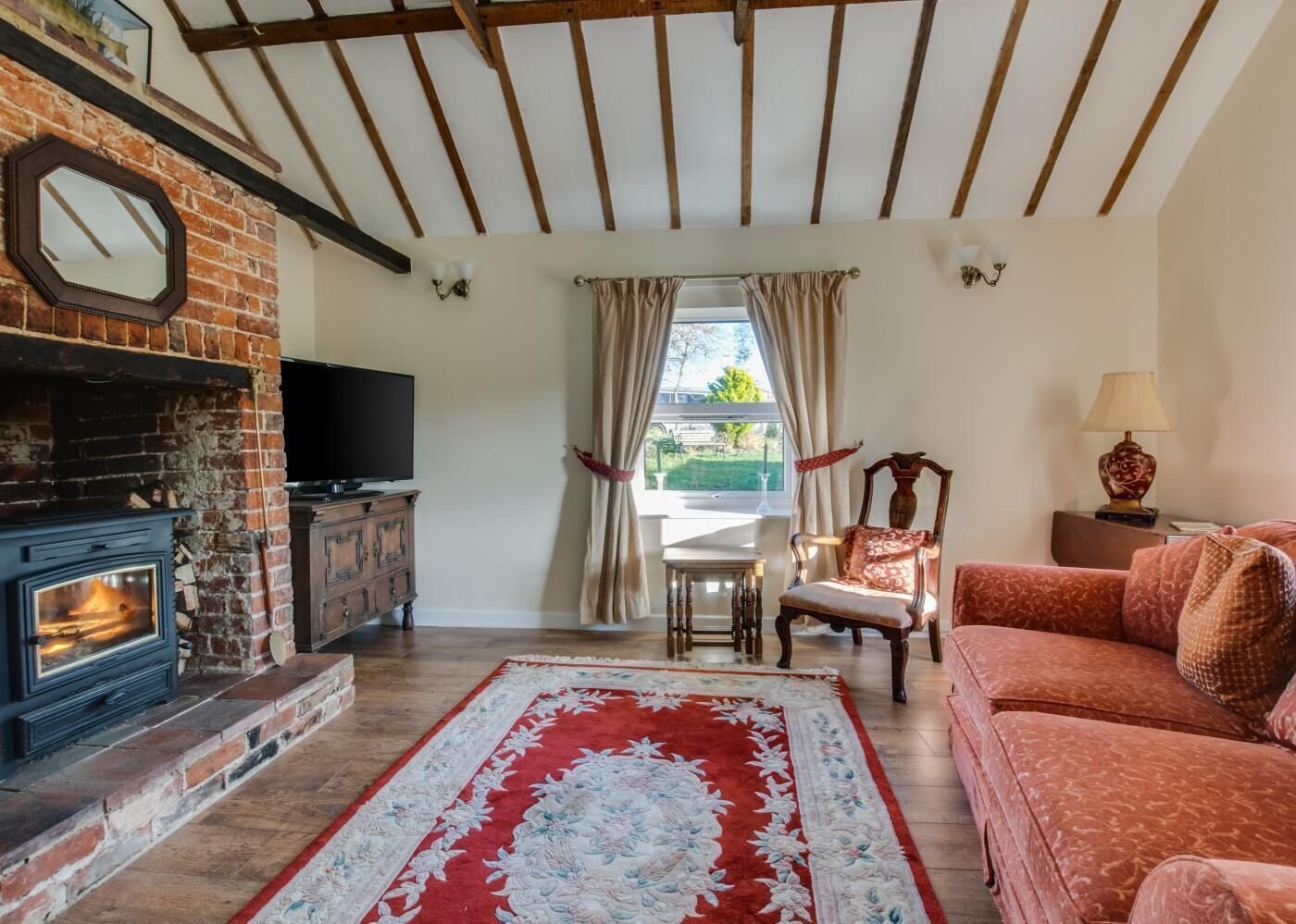 A living room with a fireplace, a television, a sofa, a patterned rug, and a view through a window.