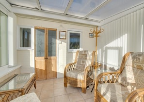 A sunlit room with a glass table, wicker chairs, a sofa, and a wooden door. - 2 Bed in Aldeburgh (oc-marsh) (Friston)