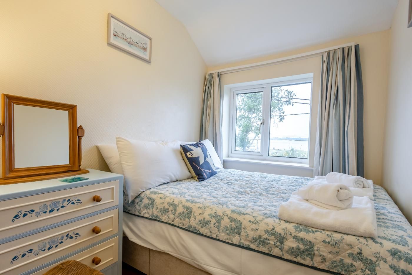 A bedroom with a bed, a dresser, a window with curtains, and a framed picture on the wall.