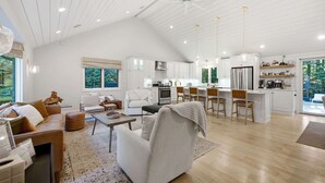 A spacious living area with a high ceiling, a kitchen with white cabinetry, and a dining area with bar stools. - Loma House - Pool, Hot Tub & Sauna walk to Lake MI (Sawyer)