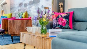 A modern living room with a grey sofa, a wooden coffee table with white cups, a vase with flowers, and a colorful floral pillow. - 2 Bed in Padstow (oc-p00714) (Padstow)
