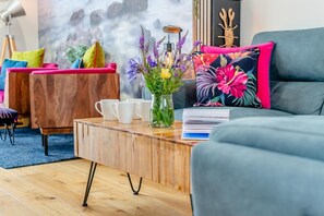 A modern living room with a grey sofa, a wooden coffee table with white cups, a vase with flowers, and a colorful floral pillow. - 2 Bed in Padstow (oc-p00714) (Padstow)