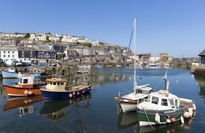 A harbor with boats docked, a clear sky, and buildings on a hillside in the background. - 5 Bed in Mevagissey (oc-p00699) (Mevagissey)