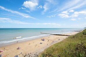 A beach with a wooden pier extending into the water, sandy beach, and a grassy cliff. - 5 Bed in Overstrand (oc-1922) (Overstrand)