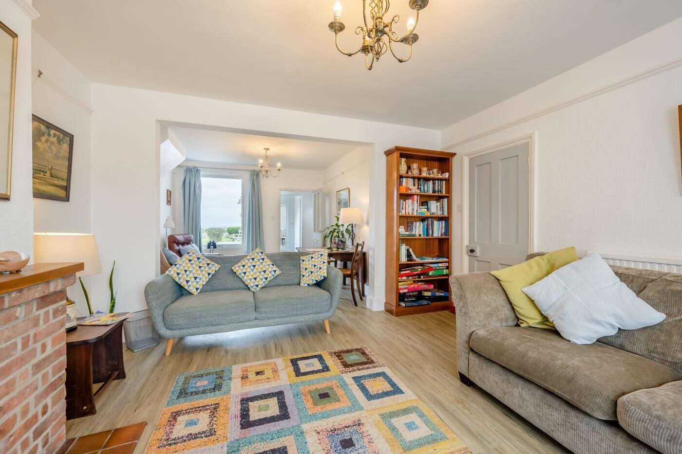 A living room with a grey sofa, a brown sofa, a patterned rug, a bookshelf, and a chandelier.
