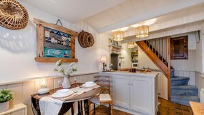 A dining area with a wooden table set for four, a kitchen with white cabinets, and a staircase leading to another level. - 1 Bed in St Ives (oc-lhse) (St Ives)