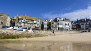 A coastal building with multiple stories, a sandy beach in the foreground, and a clear blue sky. - 1 Bed in St Ives (oc-lhse) (St Ives)