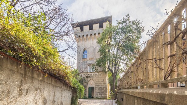 Un étroit sentier mène à un bâtiment historique en pierre, doté d’une porte verte et de fenêtres en arc de cercle.