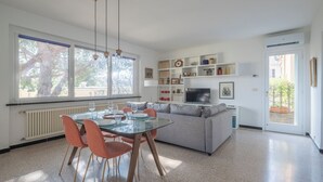 Un salon moderne avec une table à manger en verre, des chaises orange, un canapé gris et un téléviseur.
