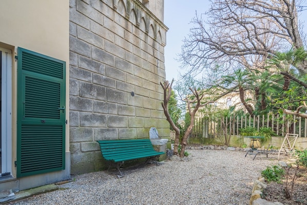 A courtyard with a green bench, a stone wall, and a gravel path.