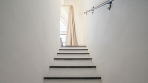 Un escalier avec une rampe métallique et un rideau beige en haut.