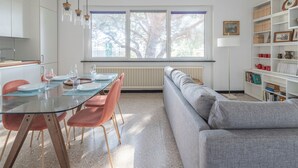Un salon moderne avec une table à manger en verre, des chaises rouges, un canapé gris et une bibliothèque.