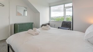 Ett hotellrum med en säng, en stol, ett element, ett fönster med utsikt och en spegel på väggen.