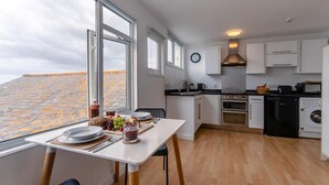 Ett modernt kök med vita skåp, ett matbord med frukost uppdukad och stora fönster.