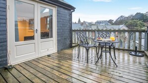 A wooden deck with a table and chairs, a white door, and a view of buildings in the background. - 1 Bed in St Ives (oc-decke) (Saint Ives)
