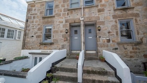A stone building with a grey door and windows, a staircase leading to the entrance, and a sign above the door. - 2 Bed in St Ives (oc-pmho10) (St Ives)