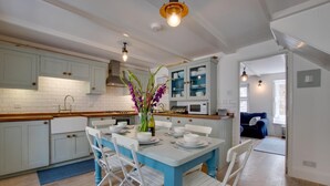 Una cocina con armarios blancos, una mesa de comedor azul y sillas blancas. Hay un jarrón con flores sobre la mesa.