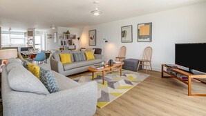 Een moderne woonkamer met een bank, salontafel, stoelen, een televisie en een boekenkast.