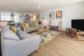 Ein modernes Wohnzimmer mit Sofa, Couchtisch und Sesseln, einem Fernseher und einem Bücherregal.