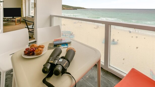 Een balkon met een ontbijttafel, een verrekijker en uitzicht op het strand.