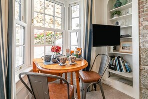 A cozy room with a round wooden table, a chair, a television on a shelf, and a bookshelf with books and decorative items. - 2 Bed in St Ives (oc-albt02) (St Ives)