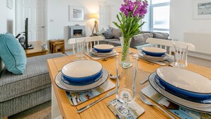 A dining area with a wooden table set for four, blue plates, a clear glass vase with purple flowers, and a framed picture on the wall. - 2 Bed in St Ives (oc-trev2) (Saint Ives)