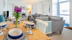 A modern living room with a dining area, a grey sofa, and a fireplace. - 2 Bed in St Ives (oc-trev2) (Saint Ives)
