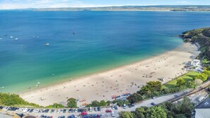 En vy över en strand sedd från luften, med en parkeringsplats och en väg som leder ner till stranden.