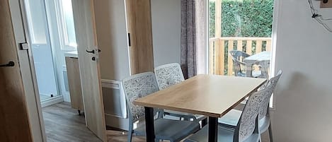 A dining area with a wooden table and chairs, a small wooden side table, and a view of a balcony with a table and chairs.