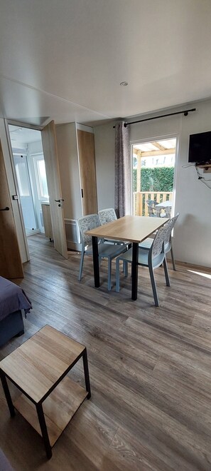 A dining area with a wooden table and chairs, a small wooden side table, and a view of a balcony with a table and chairs. - Salsa Confort (Les Mathes)