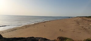 A wide sandy beach with gentle waves, a clear sky, and distant structures. - Salsa Confort (Les Mathes)