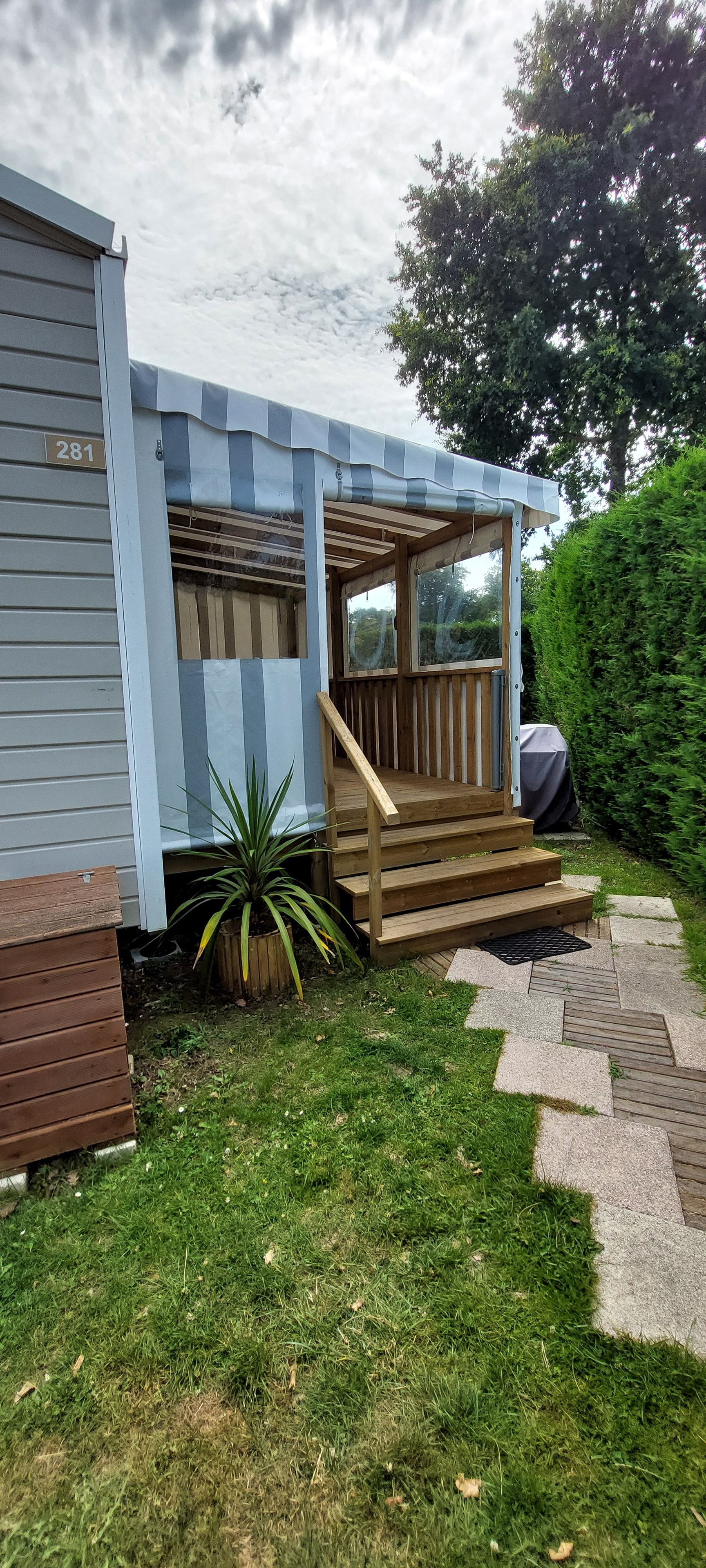 A mobile home with a wooden porch, a small garden, and a paved pathway.