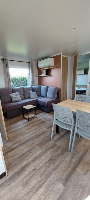 A modern living room with a sofa, a small table, and a dining area with chairs. - Salsa Confort (Les Mathes)