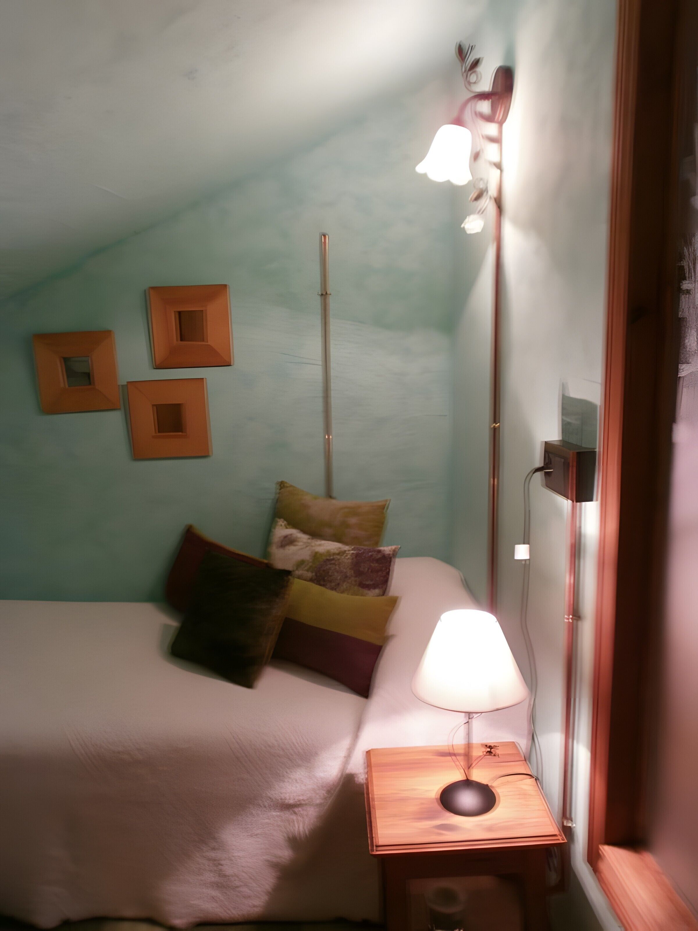 Une chambre avec un lit, une table de chevet avec une lampe et trois cadres carrés accrochés au mur.