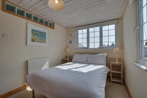 A bedroom with a bed, two bedside tables with lamps, a window with a view, and a radiator. - 1 Bed in St Ives (oc-crab03) (St Ives)