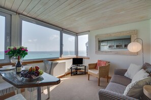A cozy room with a large window, a table with fruit, a TV, and a wicker sofa. - 1 Bed in St Ives (oc-crab03) (St Ives)