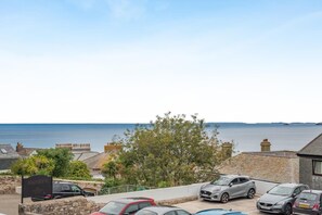 A coastal residential area with parked cars, a stone wall, and a view of the sea. - 1 Bed in St Ives (oc-clear2) (Saint Ives)