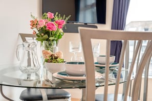A dining table set with glassware, plates, and a pitcher, with a vase of flowers in the background. - 1 Bed in St Ives (oc-clear2) (Saint Ives)