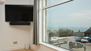 Una habitación con un ventanal grande, televisor montado y vista a coches estacionados y edificios.