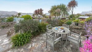 A round wooden table with chairs, surrounded by various plants and a stone wall. - 1 Bed in St Ives (oc-barn27) (Saint Ives)