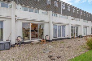 Un immeuble d’appartements moderne doté de grandes portes-fenêtres coulissantes, d’une allée en gravier et d’un espace de détente extérieur.