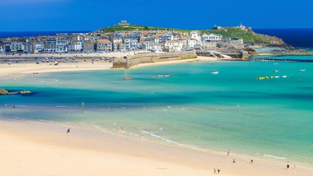 Une ville côtière dotée d’une plage de sable, d’eaux turquoise et limpides, et d’un château historique perché sur une colline.