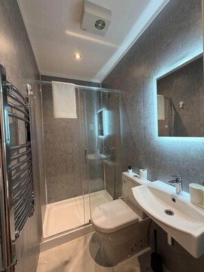 A modern bathroom with a glass-enclosed shower, a toilet, a sink, and a mirror. - Kastay: Bright London Studio | 1 Min to Trains (London)
