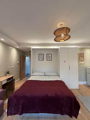 A bedroom with a bed, a desk, and a chair. There are framed pictures on the wall. - Kastay: Bright London Studio | 1 Min to Trains (London)