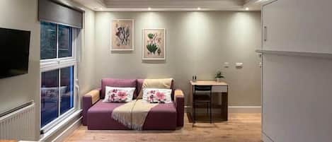 A modern living room with a sofa, a small table, a TV mounted on the wall, and a window.